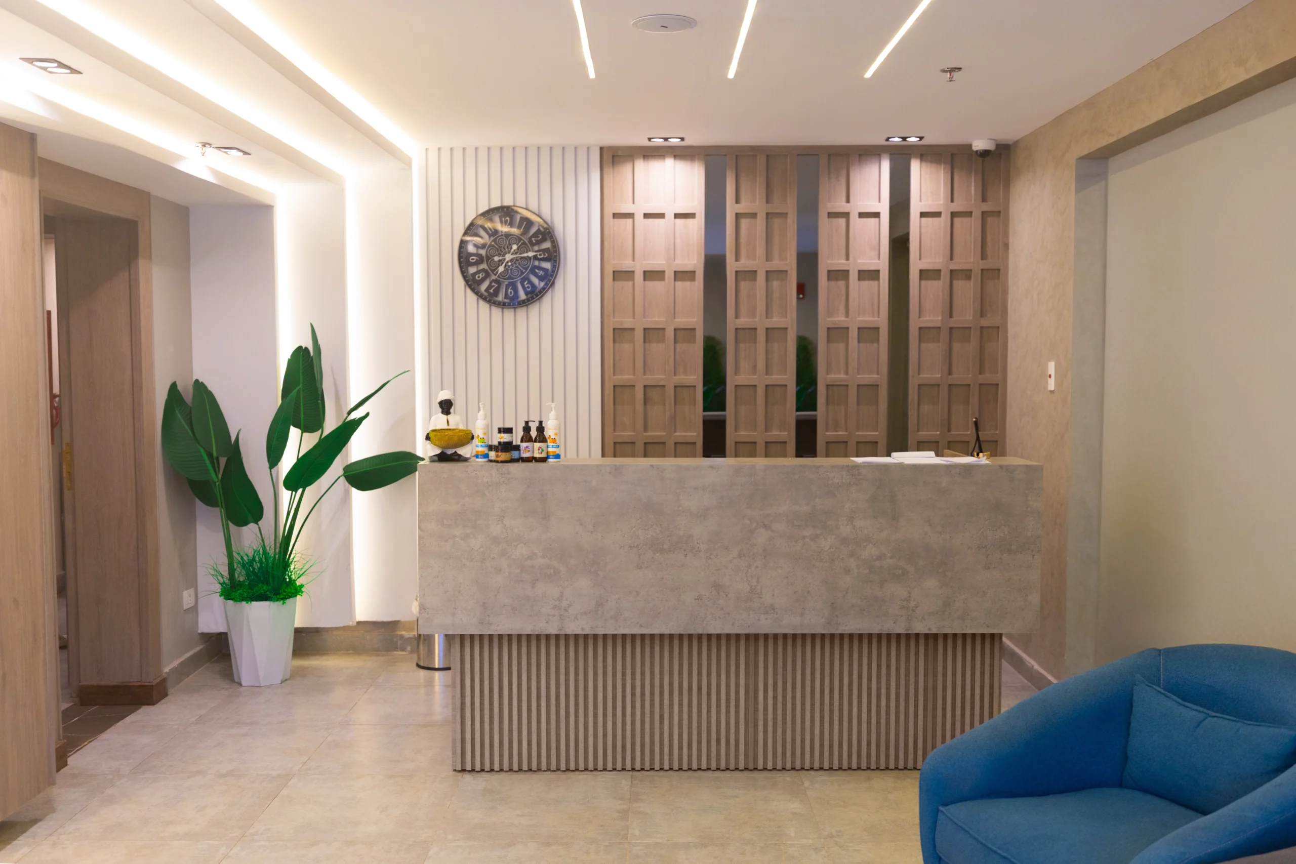 Spa reception at Flow Spectrum Sahl Hasheesh with stone-effect front desk, wooden lattice screens, tropical plant and blue armchair